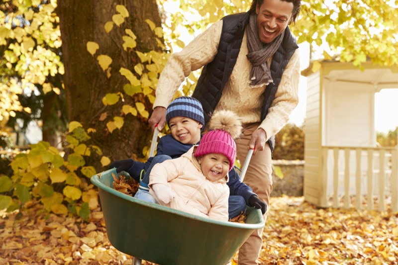 Fall HVAC Maintenance Tips to Prepare for Winter. Father In Autumn Garden Gives Children Ride In Wheelbarrow.